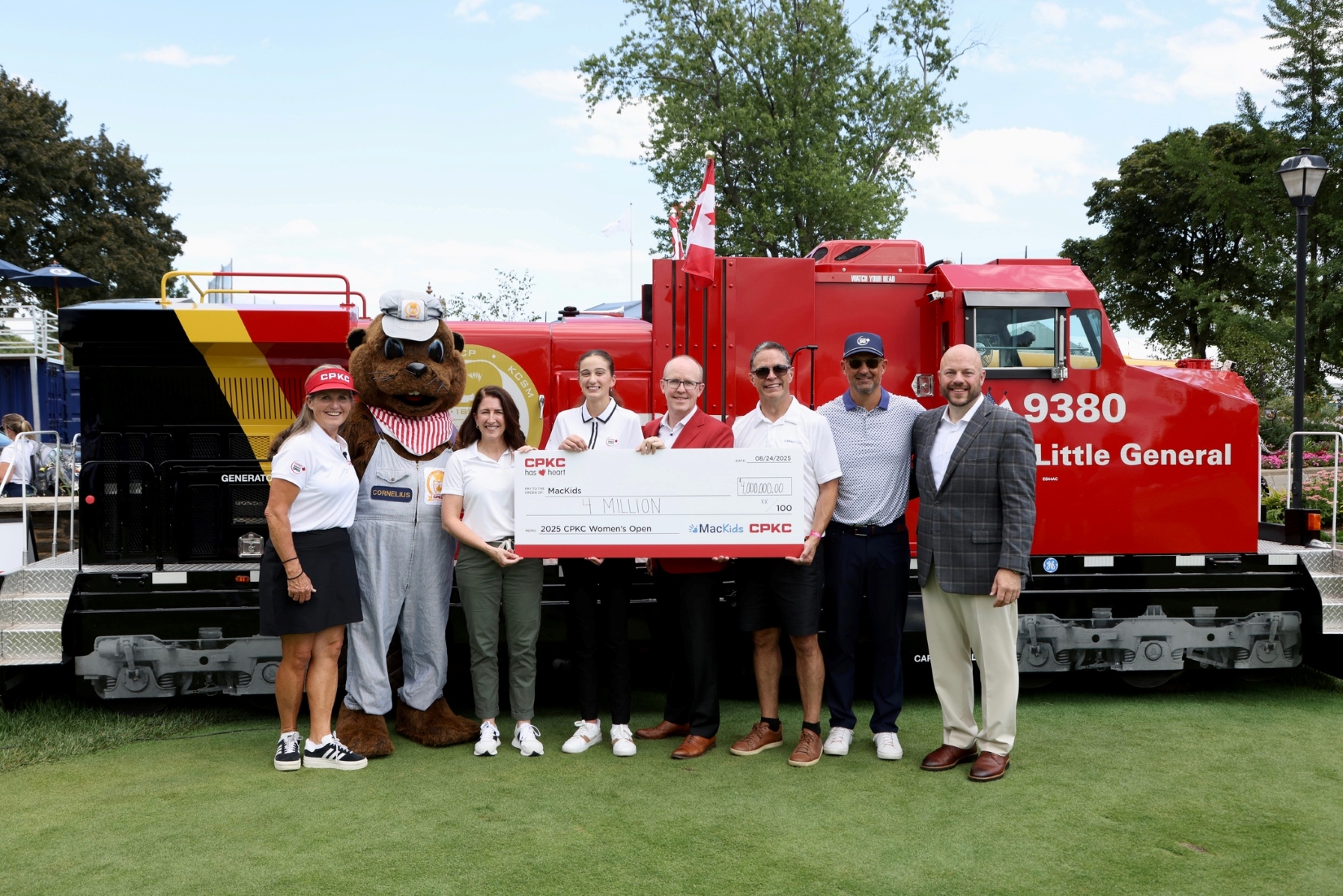 Several people holding a large novelty CPKC cheque standing in front of a red CP train engine.